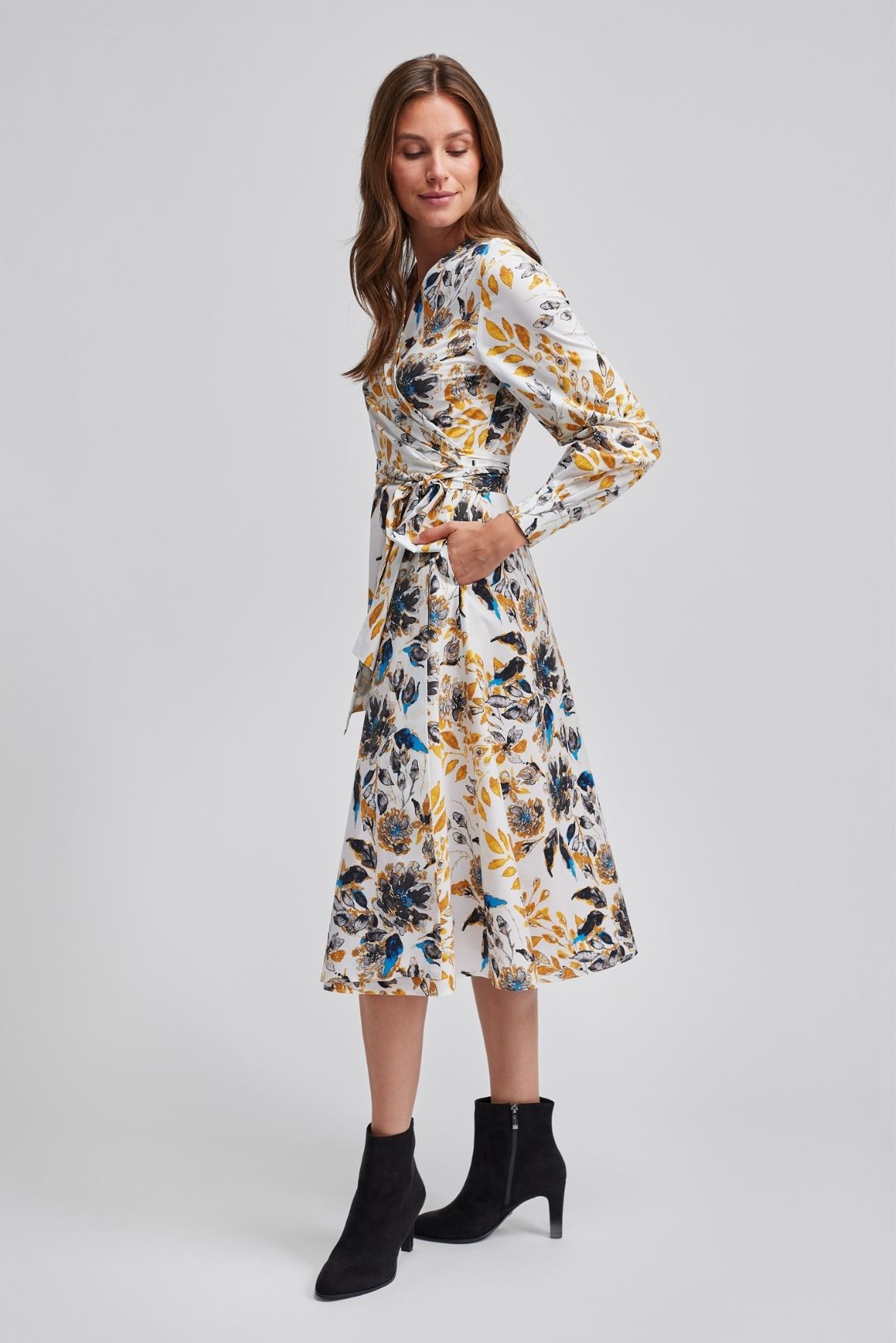 Model trägt Wickelkleid-Frühlingsfloral in Seitenansicht, taillenbetont gebunden, Rock in Midilänge.