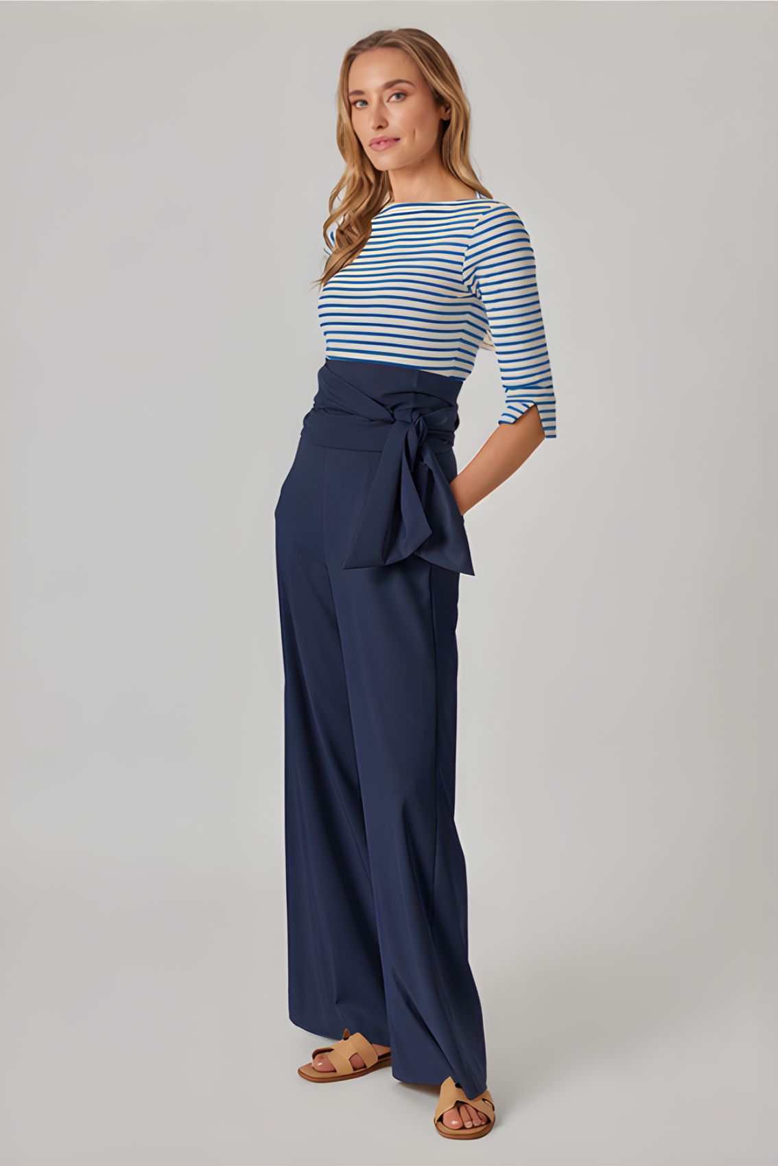 Model trägt blaue Wide-Leg Hose, Seitenansicht mit fließendem Fall und taillenbetontem Sitz durch Bindegürtel.