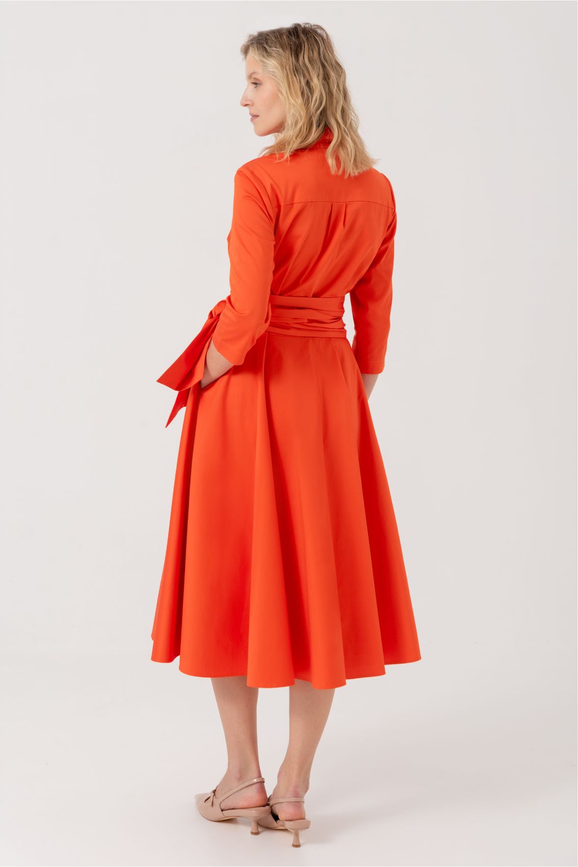 Blusenkleid mit Bindegürtel Orange: Rückansicht des eleganten A-Linien-Kleides in leuchtendem Orange, mit 3/4-Ärmeln und ausgestelltem Midi-Rock. Der breite Bindegürtel betont die Taille. Das Kleid fällt fließend bis zur Wade und zeigt die schmeichelhafte Silhouette von hinten.