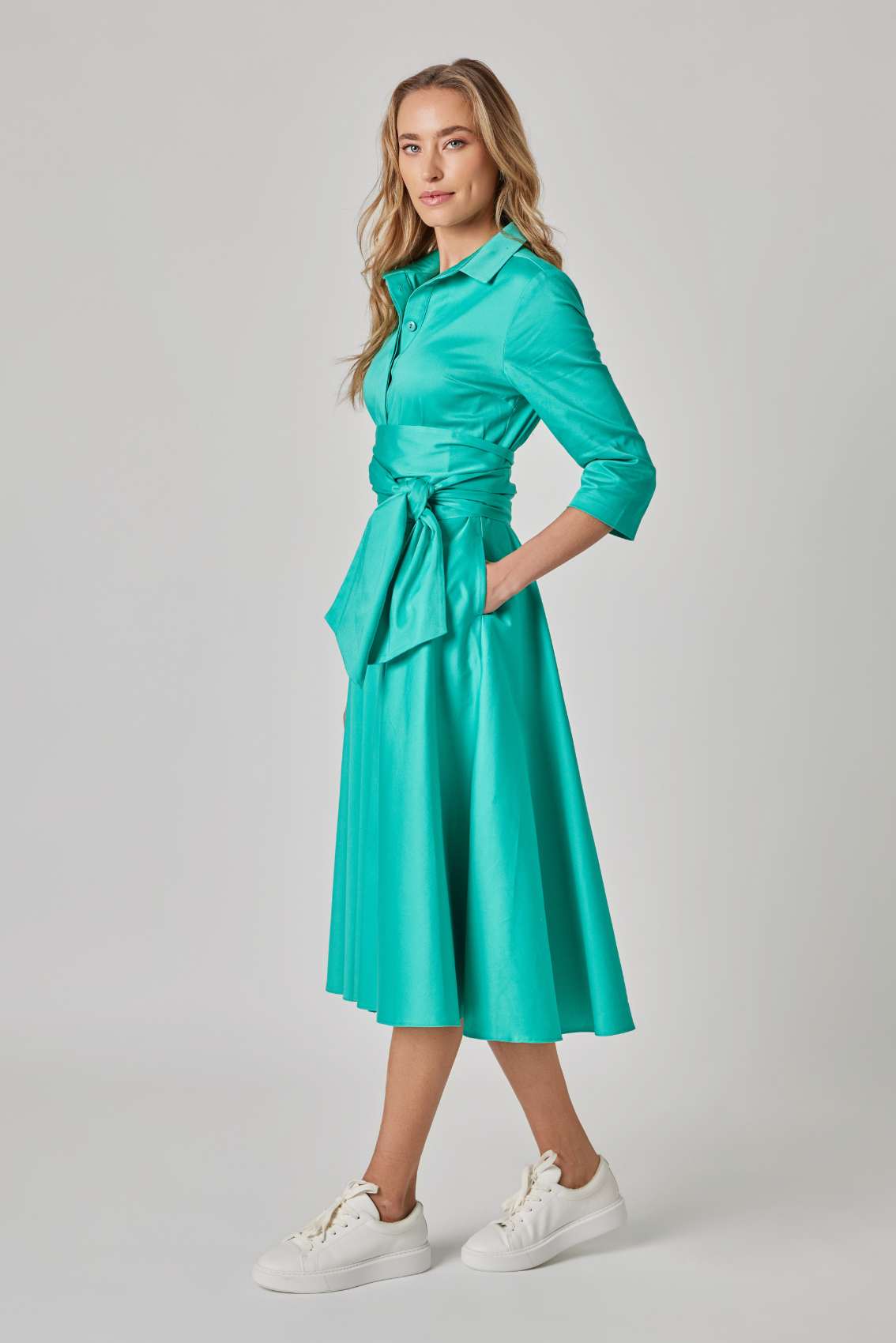Model trägt türkises Blusenkleid mit Bindegürtel und 3/4-Ärmeln, Seitenansicht.