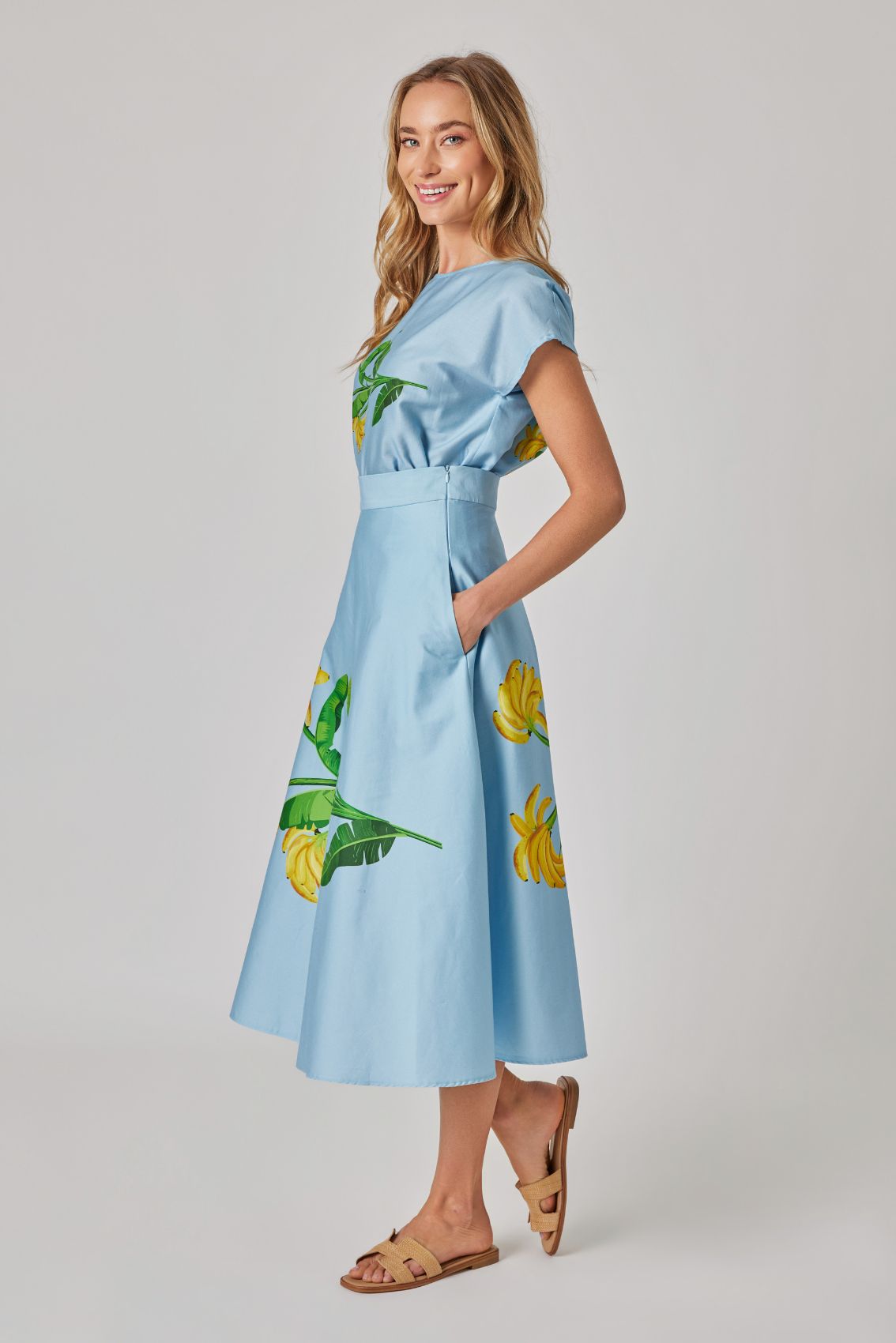 Model trägt hellblauen Midirock mit Bananen-Print in Seitenansicht, Seitentaschen sichtbar.