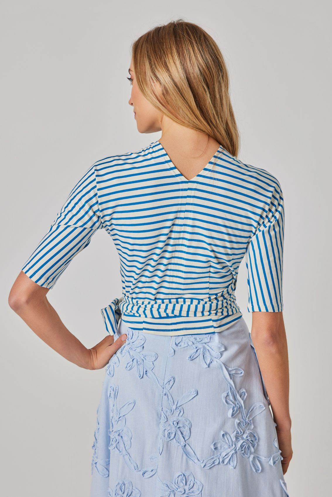 Model trägt Wickeltop blau-creme gestreift, Rückenansicht mit V-Form am Ausschnitt und Streifenmuster.