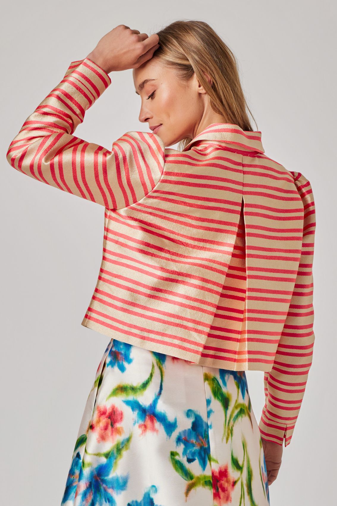 Model trägt gold-orange gestreifte Kurzjacke, Rückenansicht mit Kellerfalte und cropped Saum.