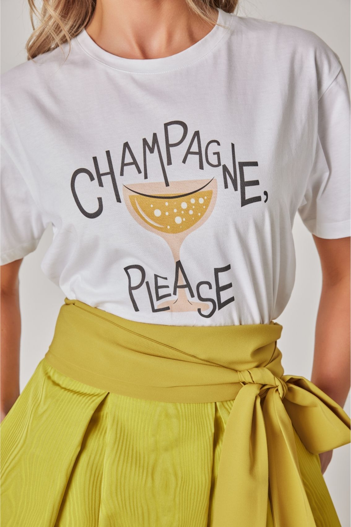 Detailansicht des Prints „Champagne Please“ mit stilisiertem Champagnerglas auf weißem T-Shirt.