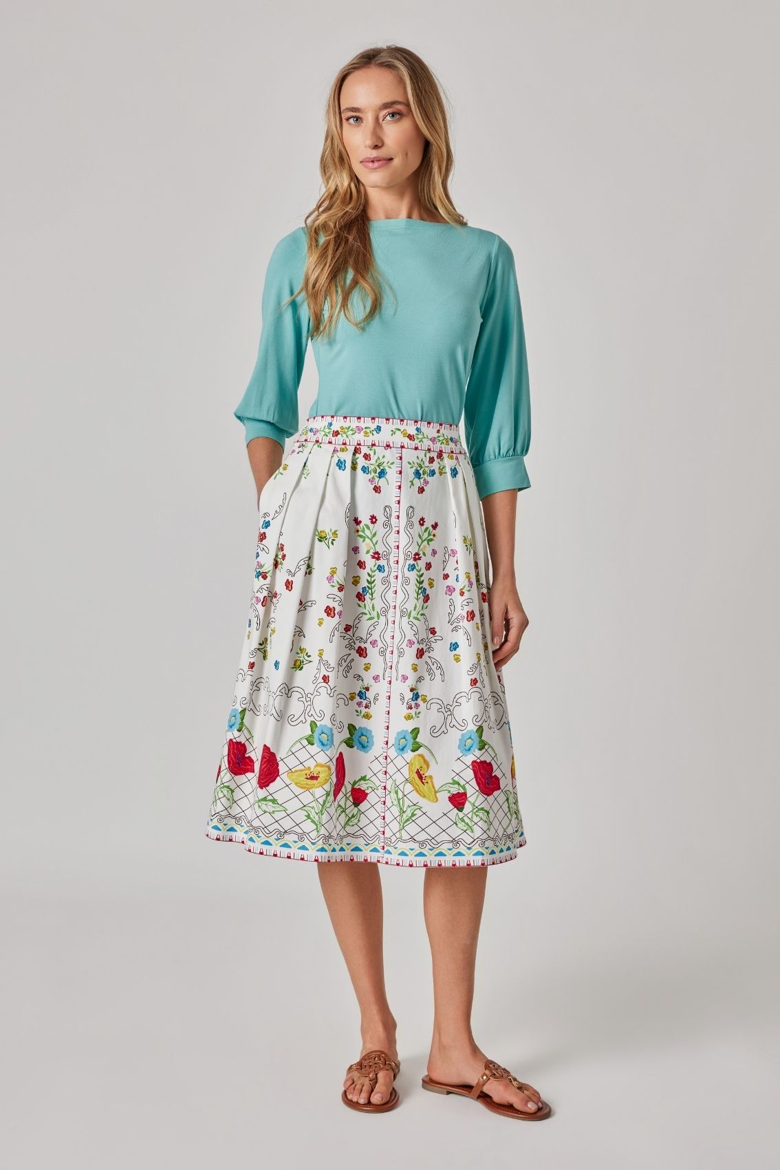 Model trägt Midirock mit Blumenprint mit ausgestellter Silhouette und Bordürenmuster am Saum, Frontansicht.