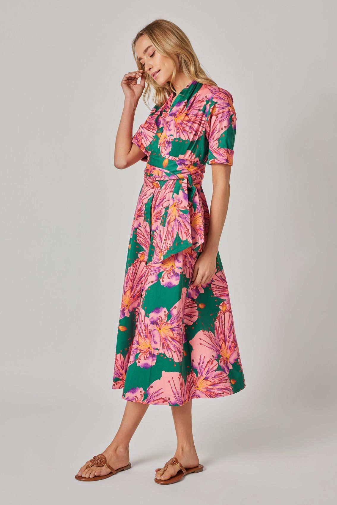 Model trägt Blusenkleid mit großem floralem Print und Bindegürtel, Seitenansicht mit leicht ausgestelltem Rockteil.