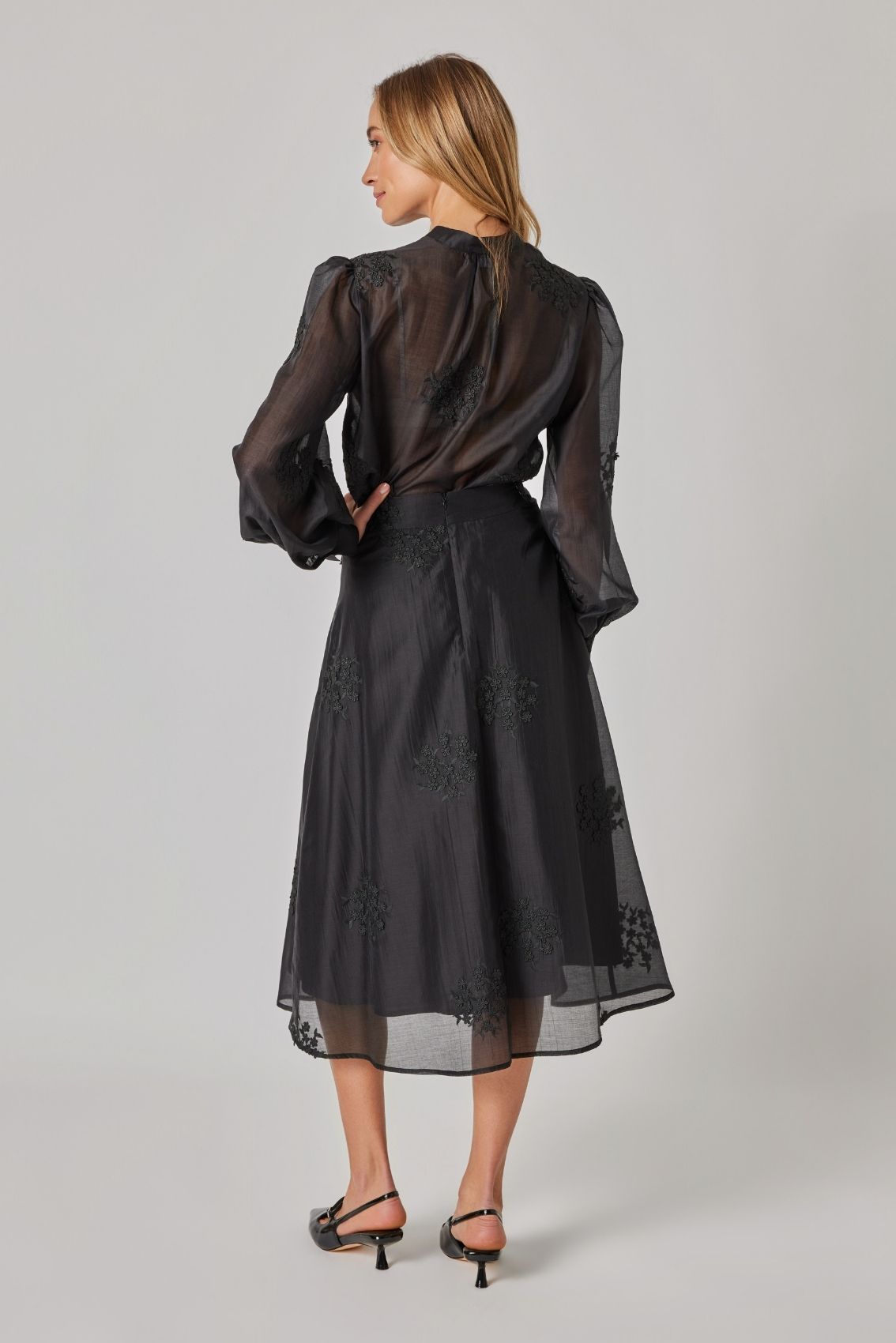 Model trägt schwarzen Midi-Rock mit floraler Stickerei und verdecktem Reißverschluss hinten, Rückenansicht.