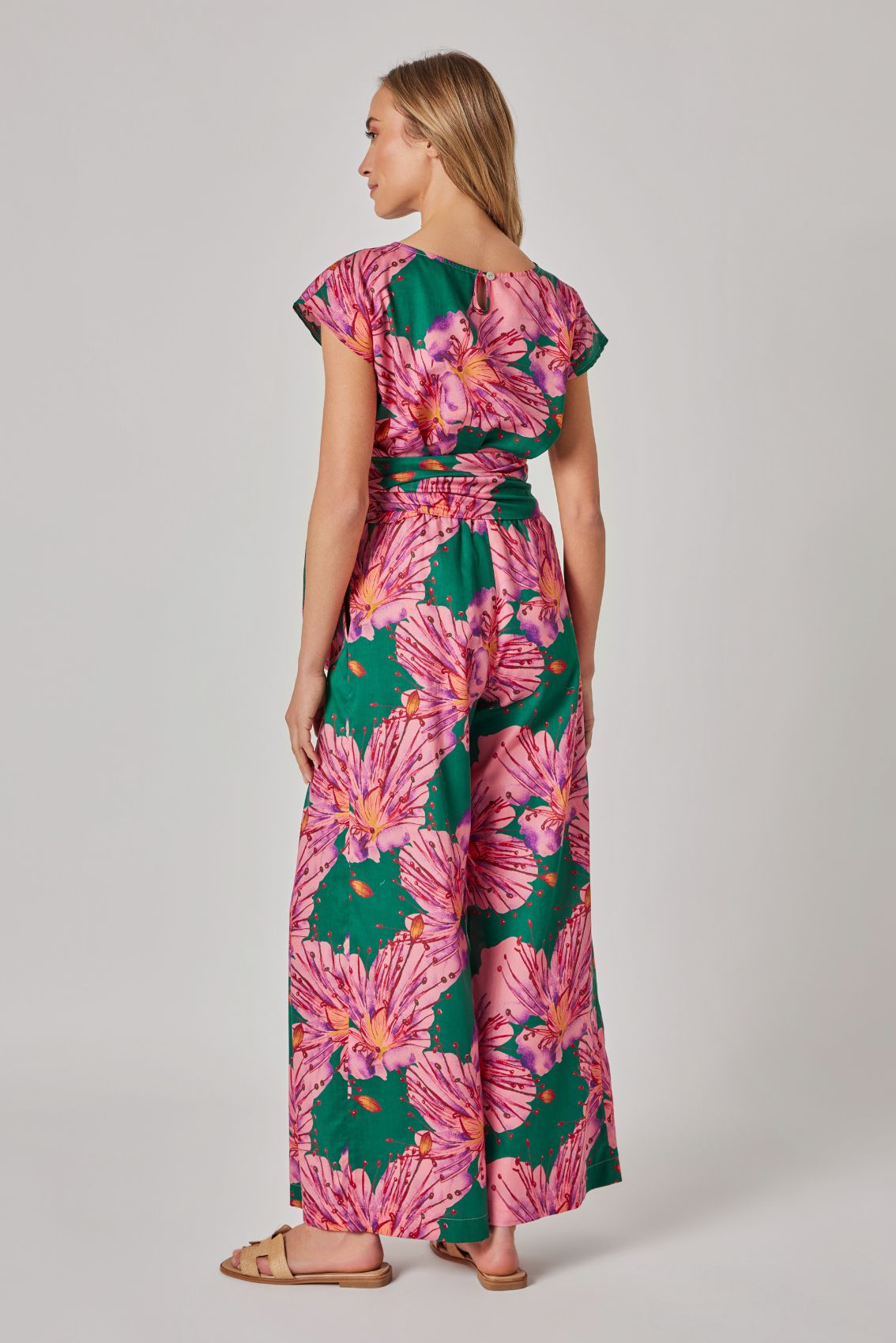 Model trägt grüne, weite Hose mit floralem Print und Wickelbund, Rückenansicht.
