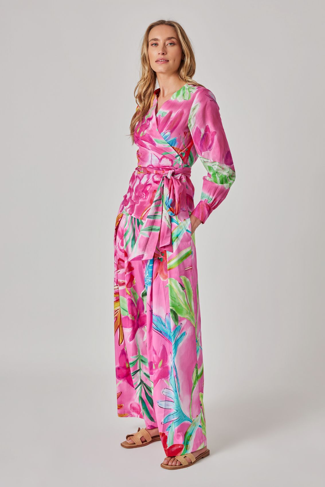 Model trägt pinke, weite Hose mit floralem Print und Wickelbund mit Bindegürtel, Seitenansicht.