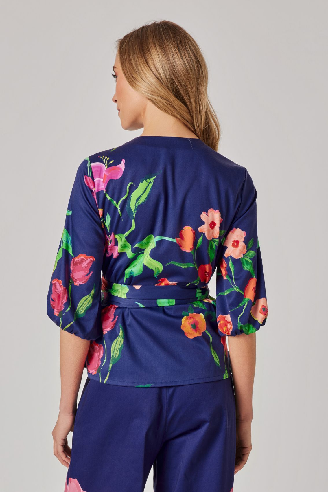 Model trägt Wickeloberteil in Dunkelblau mit floralem Print und 3/4-Ärmeln, Rückenansicht.