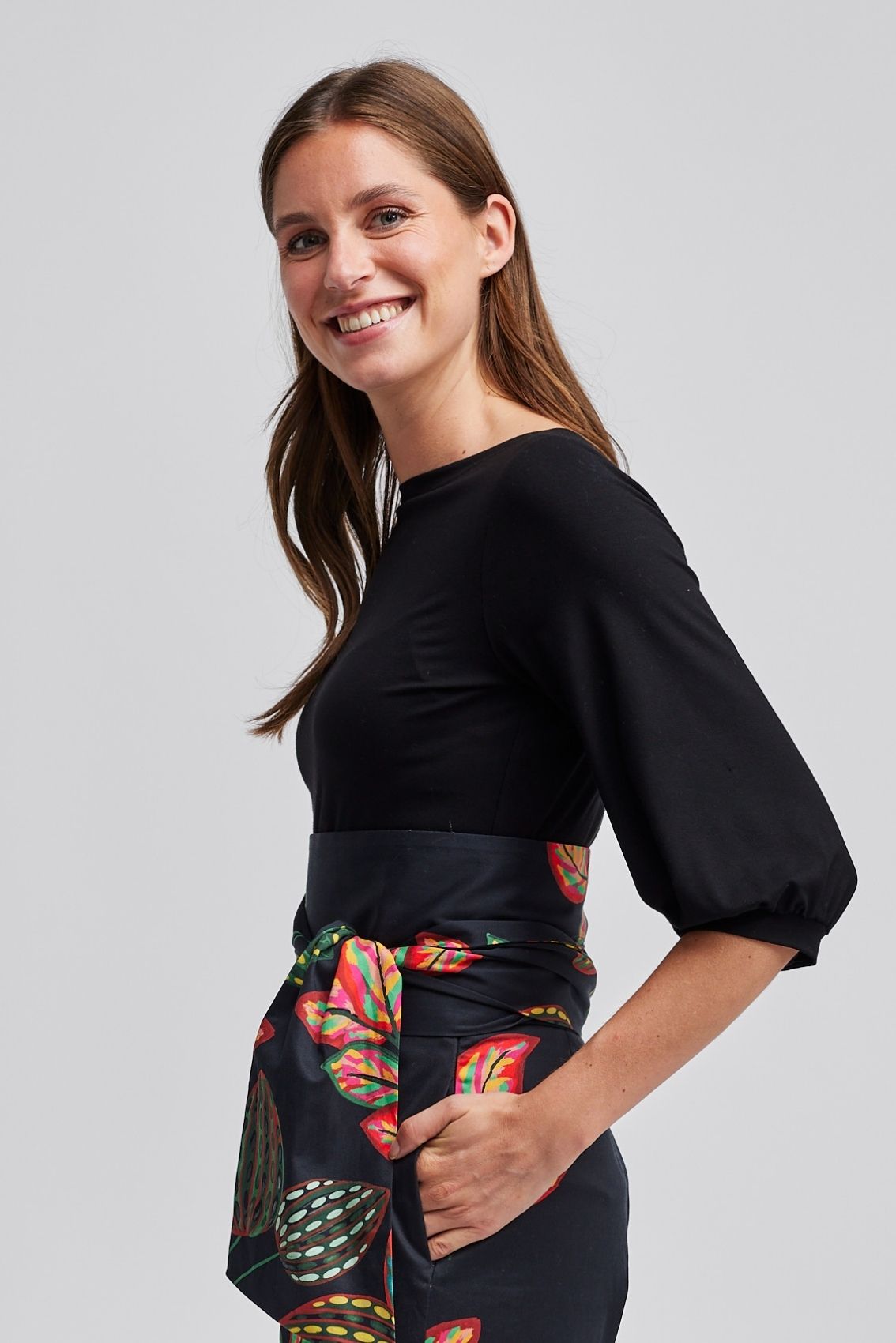 Model trägt schwarzes Shirt mit U-Boot-Ausschnitt und sehr lockeren 3/4-Ärmeln, Seitenansicht.