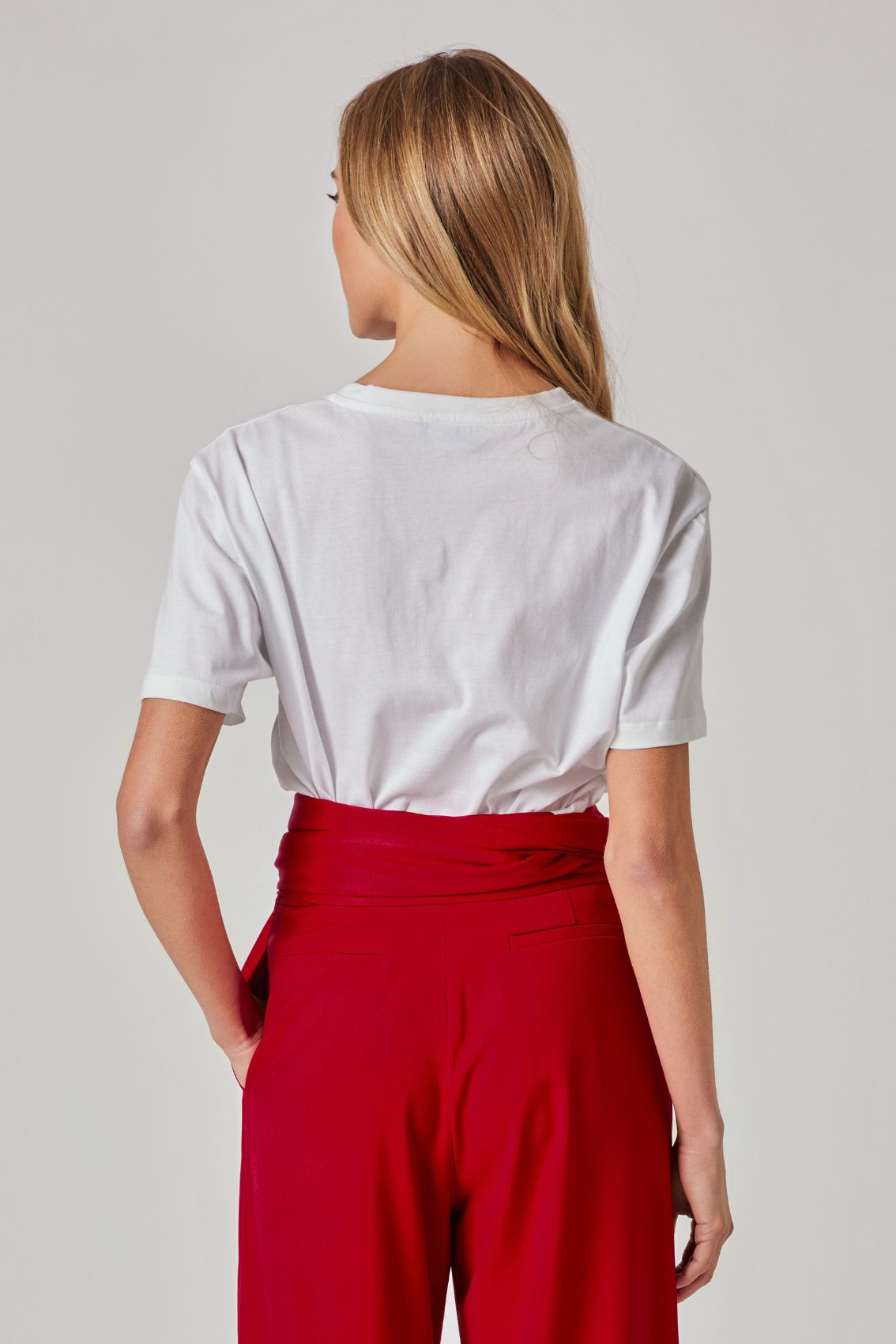 Model trägt weißes T-Shirt von hinten; rote High-Waist Hose mit Wickelbund, Rückenansicht.