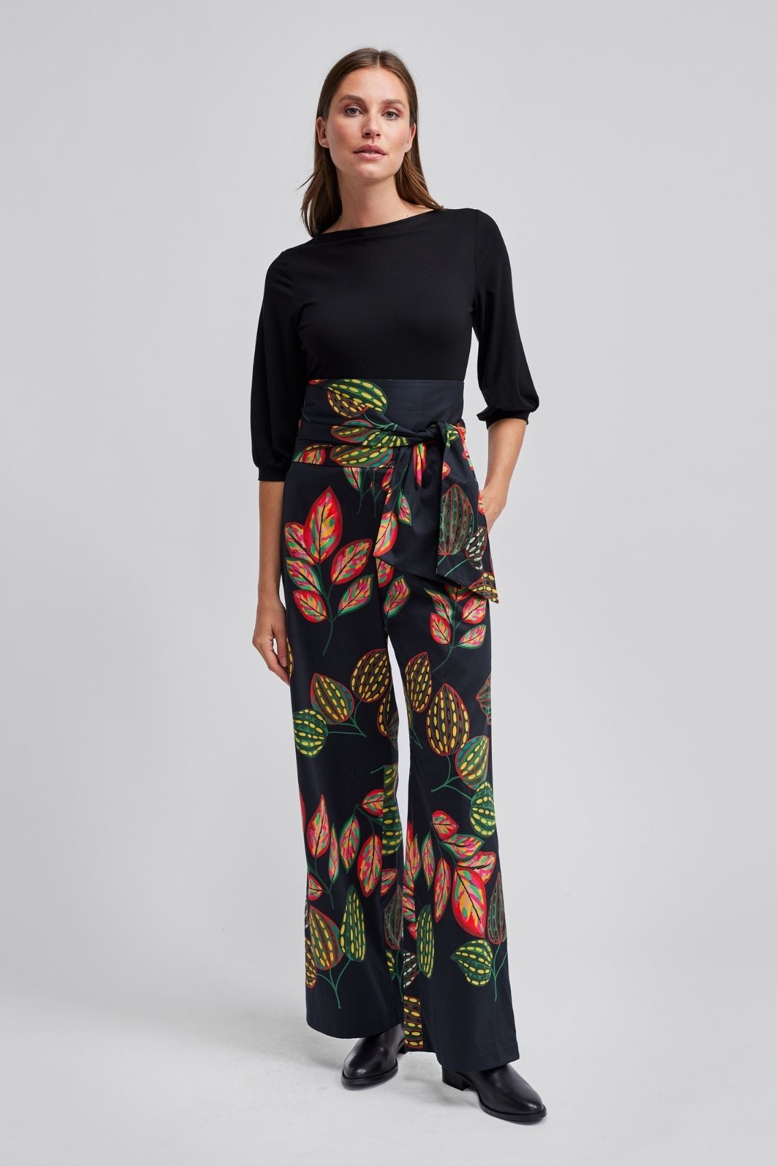 Model trägt schwarze High-Waist Hose mit weitem Bein, Bindegürtel und buntem Blätter-Print, Frontansicht.