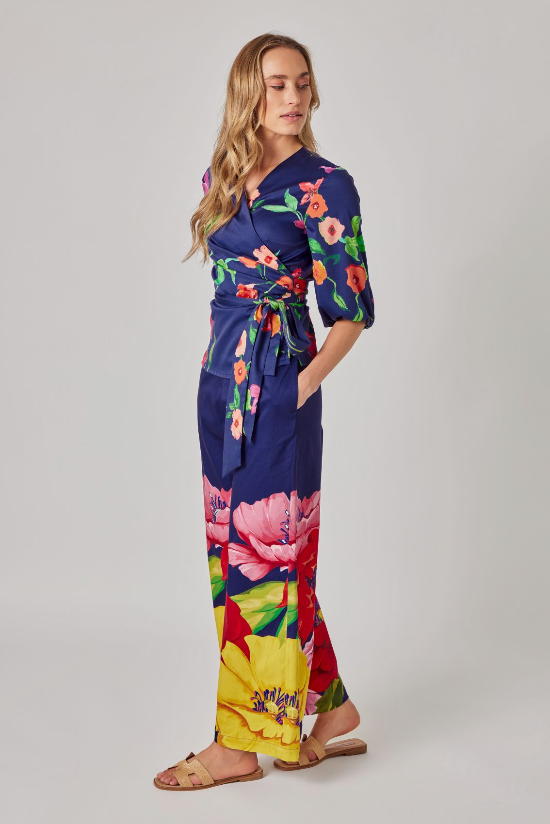Model trägt dunkelblaue Hose mit weitem Bein und großem Blumenprint am Saum, Seitenansicht.