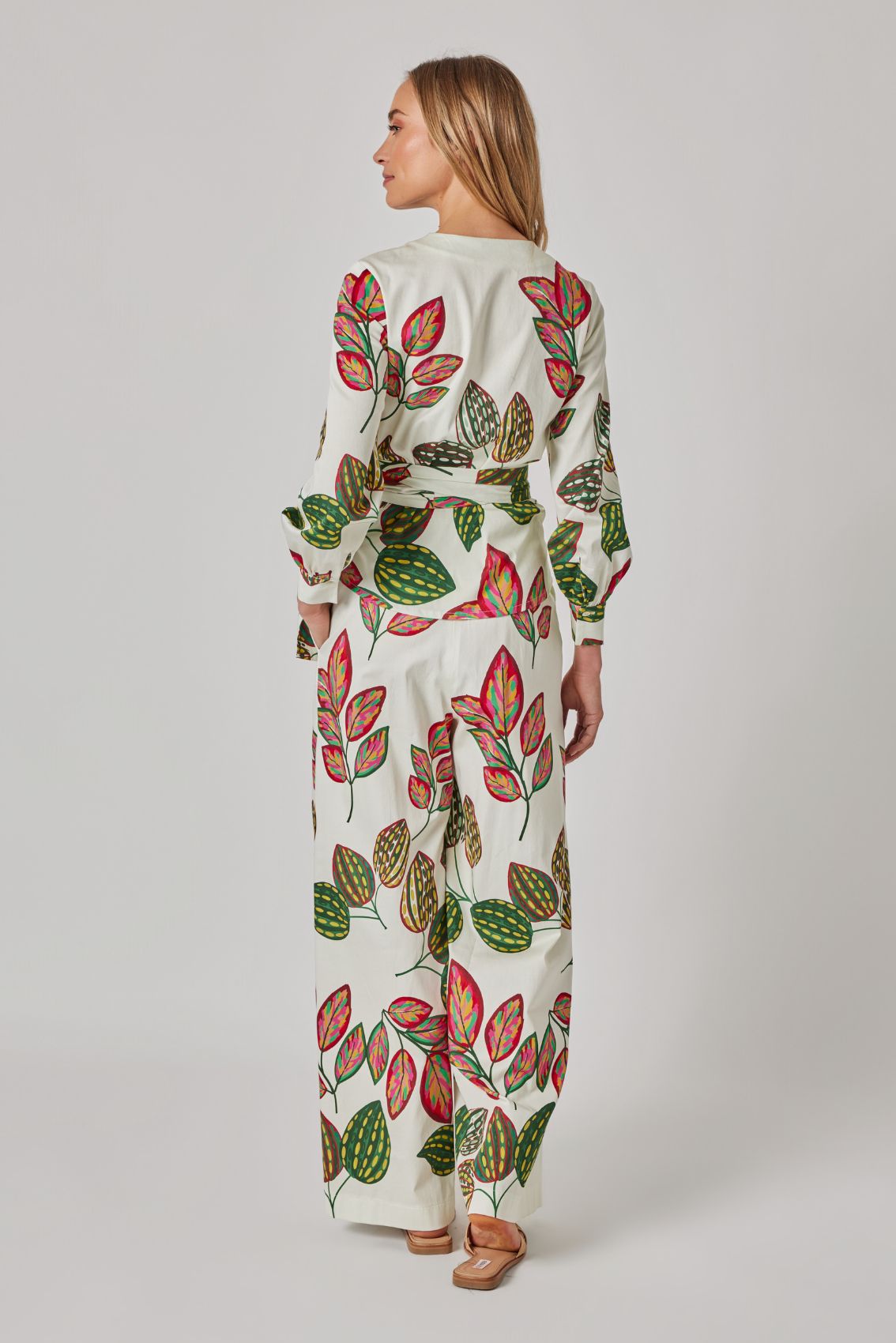 Model trägt weiße, weit geschnittene Hose mit Blattprint, Rückenansicht.