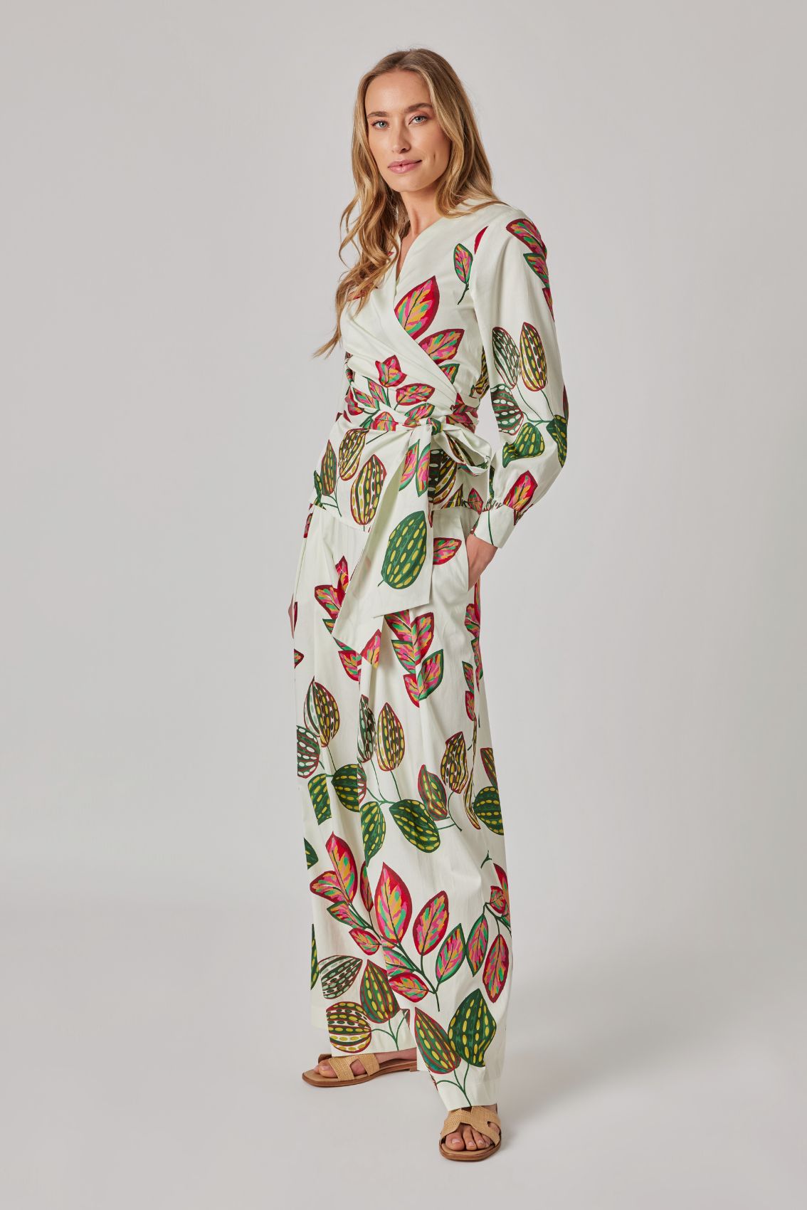 Model trägt weiße, weit geschnittene Hose mit Blattprint, Seitenansicht.