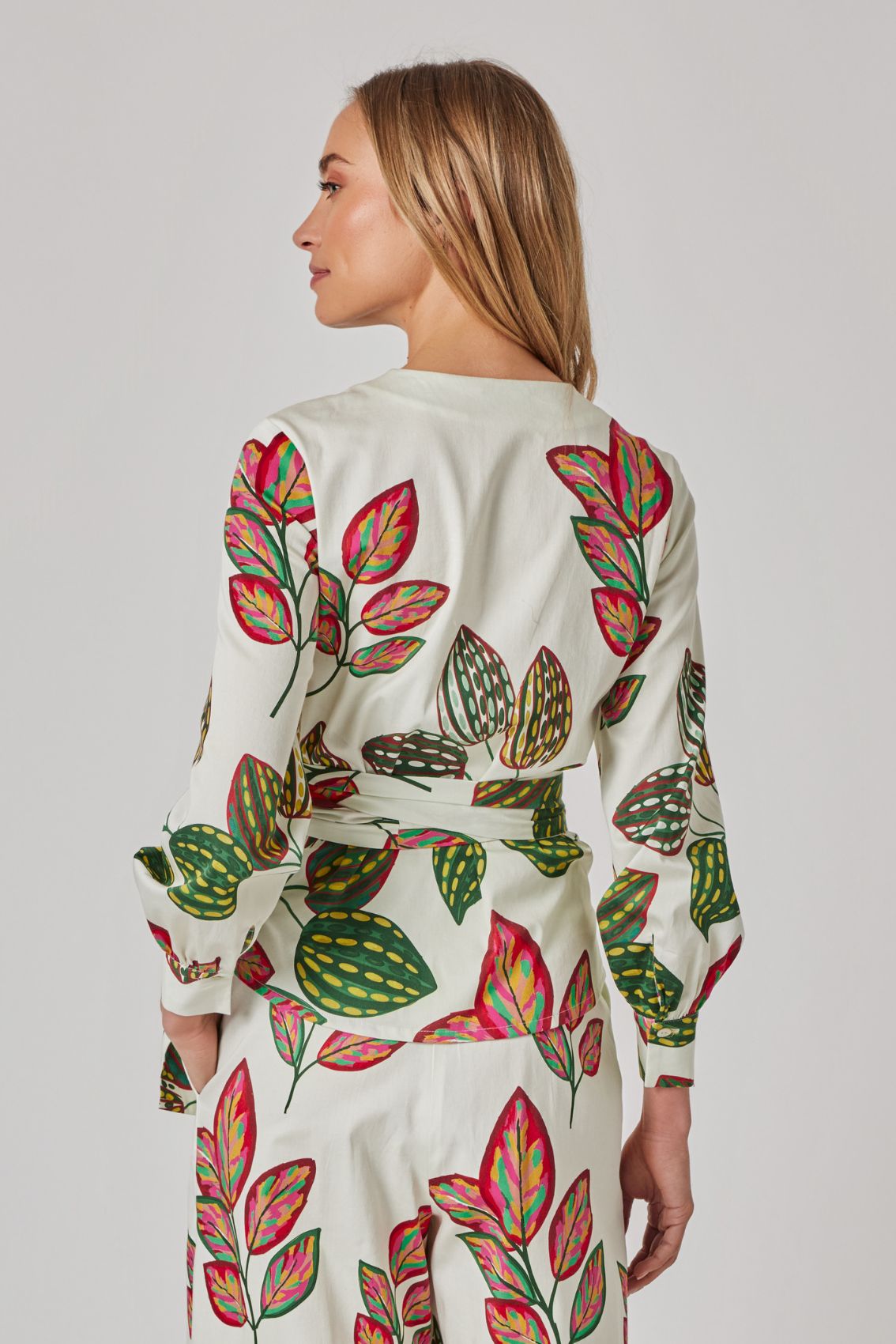Model trägt helle Hose mit weitem Bein und buntem Blätter-Print, Rückenansicht.