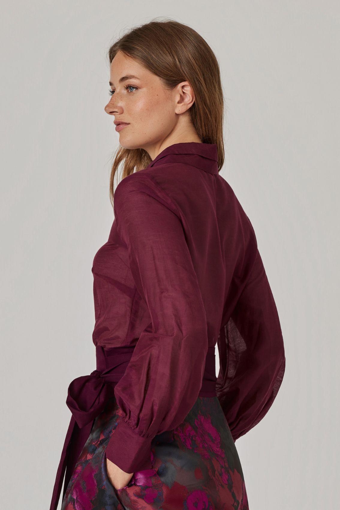 Model trägt Bluse in Aubergine mit leicht transparentem Stoff, Rückenansicht.