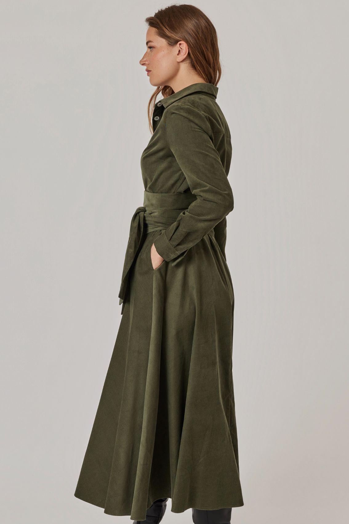 Model trägt Cordkleid in Olivgrün, Seitenansicht mit taillierendem Bindegürtel.