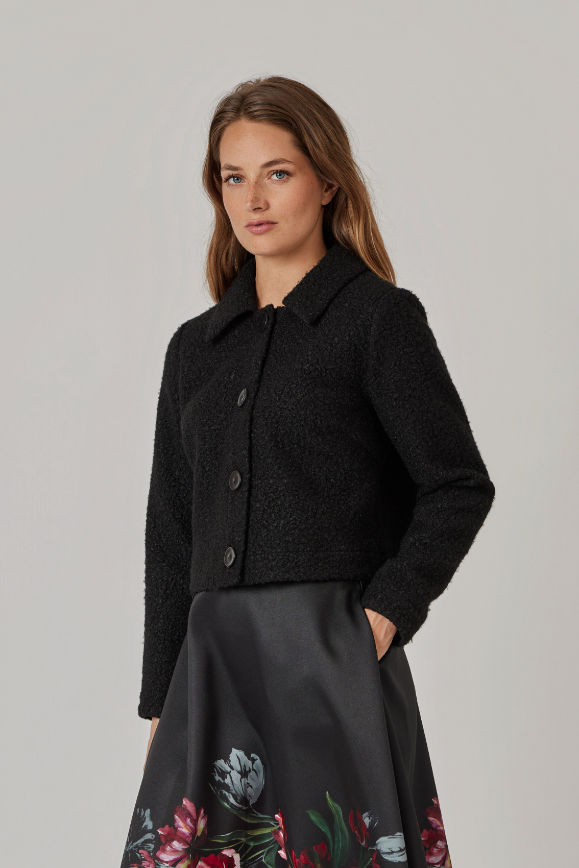 Model trägt schwarze Jacke zu Satinrock mit Blumenprint, Seitenansicht der kurzen, geraden Form.