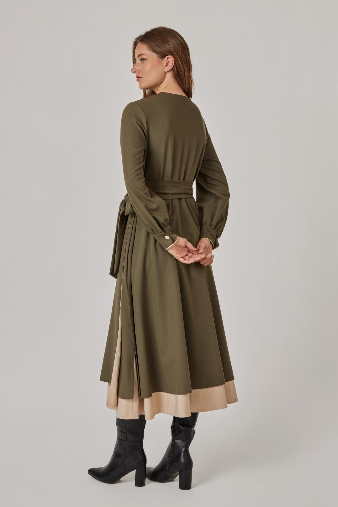Model trägt olivfarbenes Kleid mit Bindegürtel und Ballonärmeln, Rückenansicht mit Unterrock in Sand.