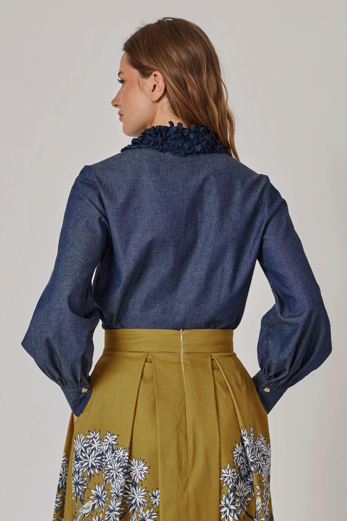 Model trägt Bluse in Denimblau, Rückansicht mit geraffter Manschette.