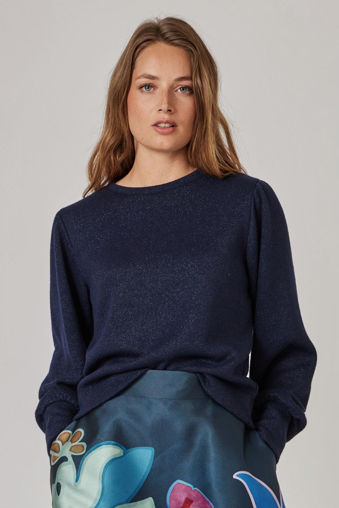 Model trägt navyfarbenen Glitzer-Strickpullover mit Puffärmeln zu bedrucktem Rock, Frontansicht.