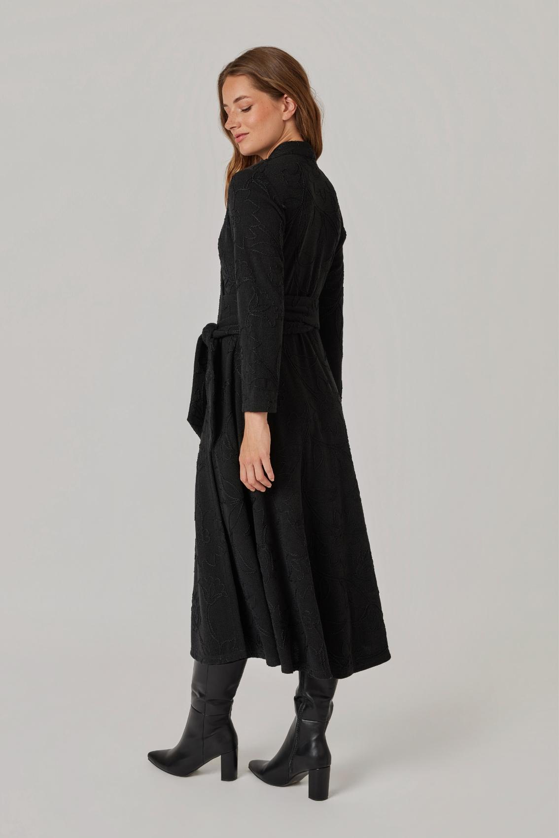 Model trägt schwarzes Kleid mit Blumenstickerei, Rückansicht mit weit ausgestelltem Rock.