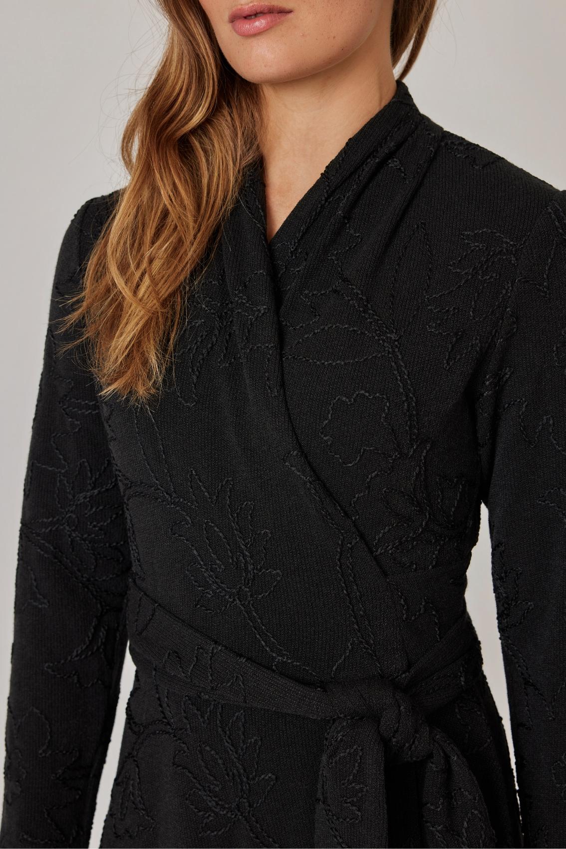 Model trägt schwarzes Kleid mit Blumenstickerei, Seitenansicht mit Schleife des Bindegürtels an der Taille.
