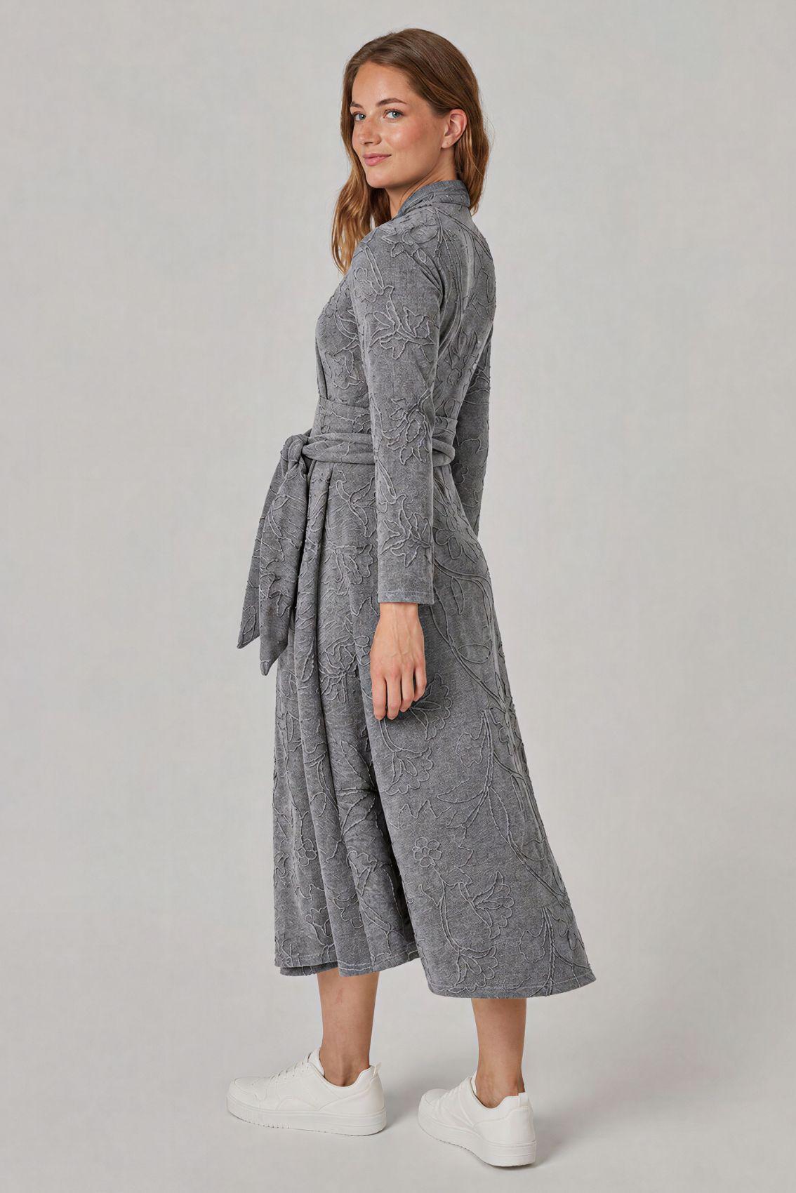 Model trägt graues Kleid mit Blumenstickerei, Seitenansicht mit Schleife des Bindegürtels an der Taille.
