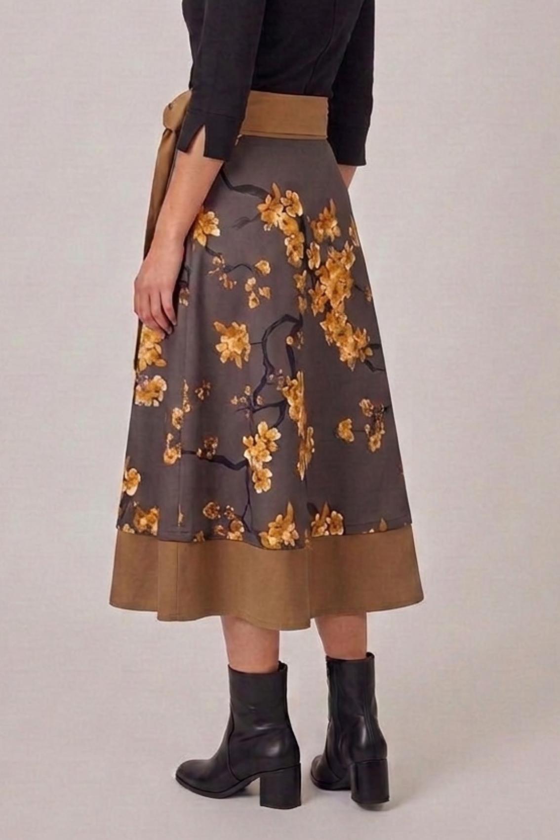 Model trägt Wickelrock mit Kirschblütenprint, Rückansicht mit breitem Saumstreifen in Karamell und schwarzen Stiefeletten.