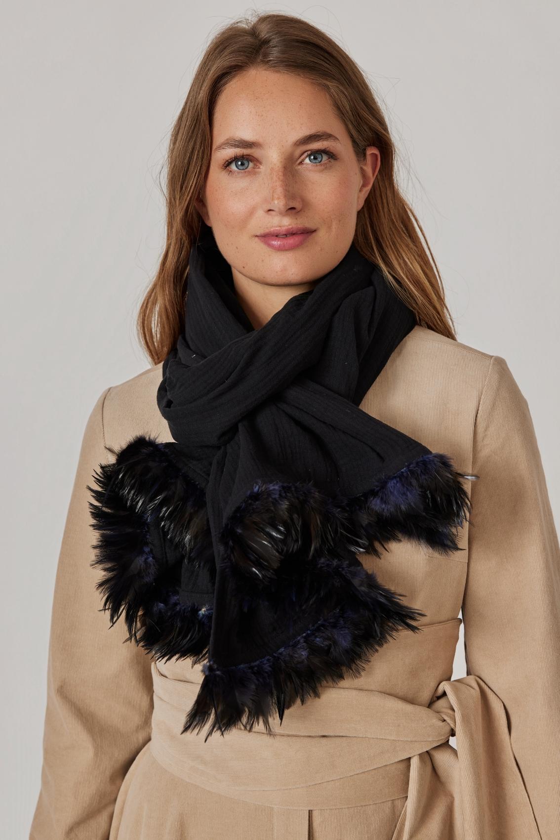 Model trägt schwarzen Musselinschal mit Federbesatz um den Hals, Frontansicht über beigem Mantel.
