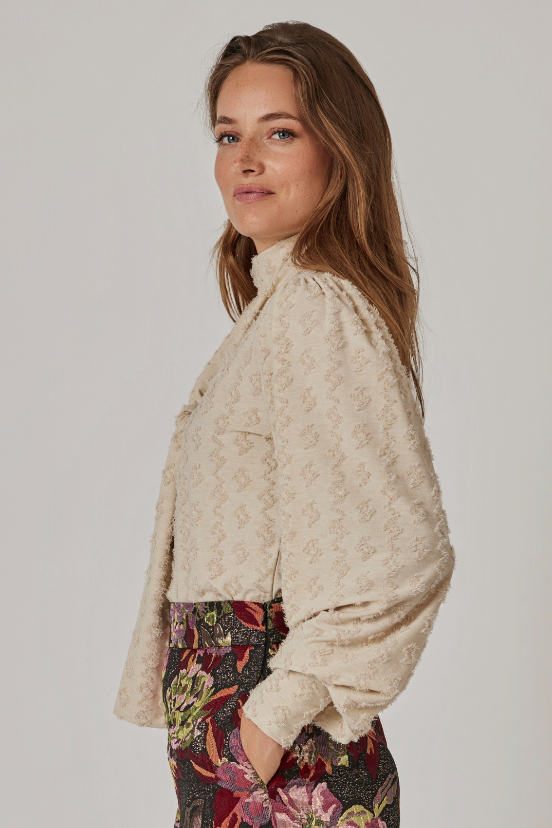 Model trägt cremefarbenes Shirt mit Rollkragen, Seitenansicht mit Ballonärmeln und gekräuselter Schulter.