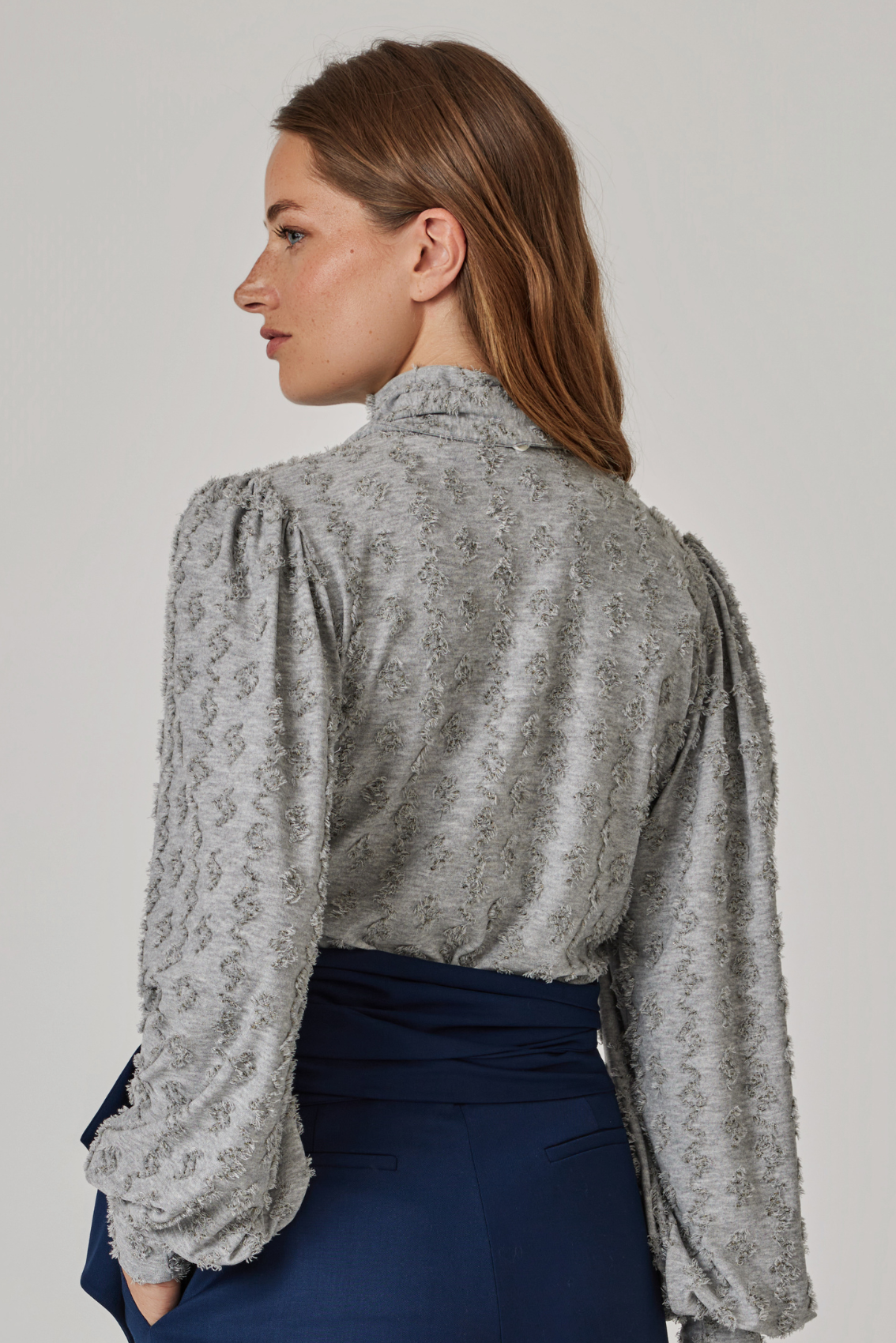 Model trägt steingraues Shirt mit Rollkragen, Rückenansicht mit gekräuselter Schulter und Struktur im Stoff.
