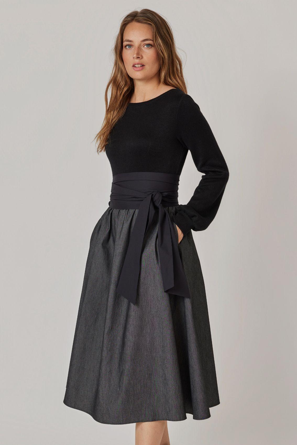 Model trägt Strick-Mix-Kleid, Seitenansicht mit tailliertem Bindegürtel und Seitentaschen.