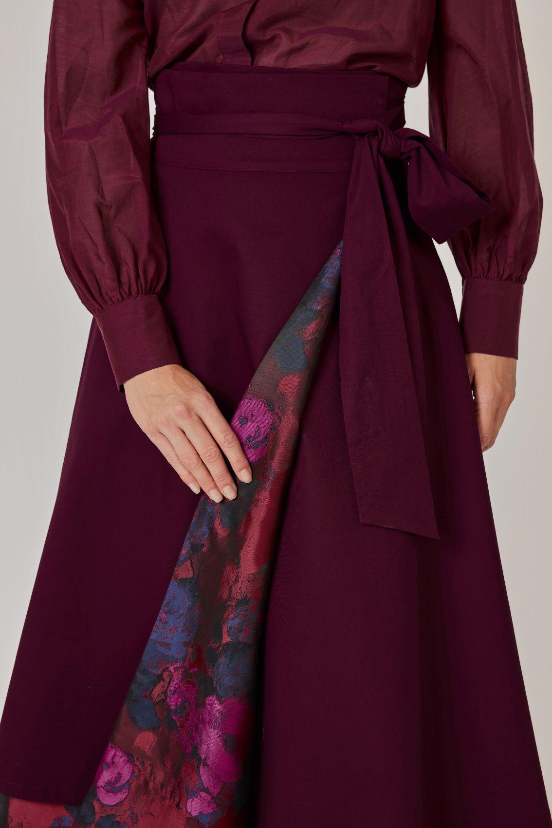 Detailansicht: Wickelkante der Aubergine-Seite leicht geöffnet, darunter Rosen-Jacquard; Bindegürtel mit Schleife.