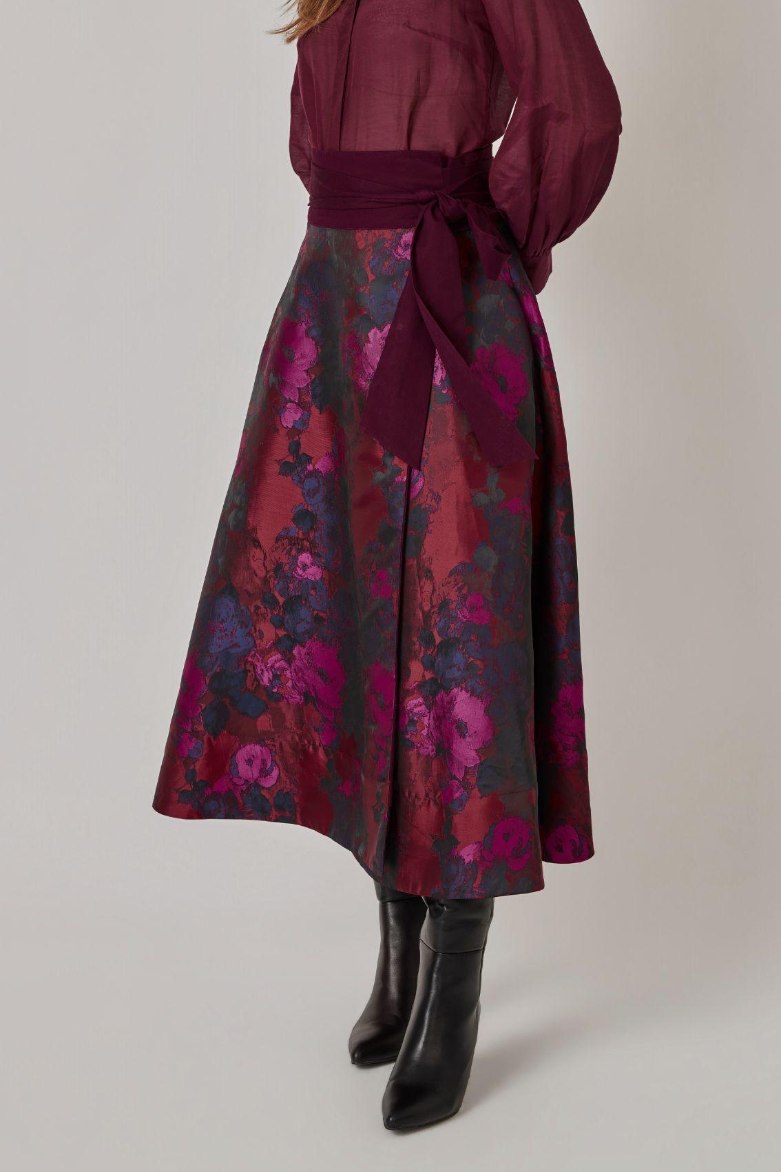 Model trägt Wickelrock mit Rosen-Jacquard und seitlich gebundener Schleife, Seitenansicht mit schwingender A-Linie.