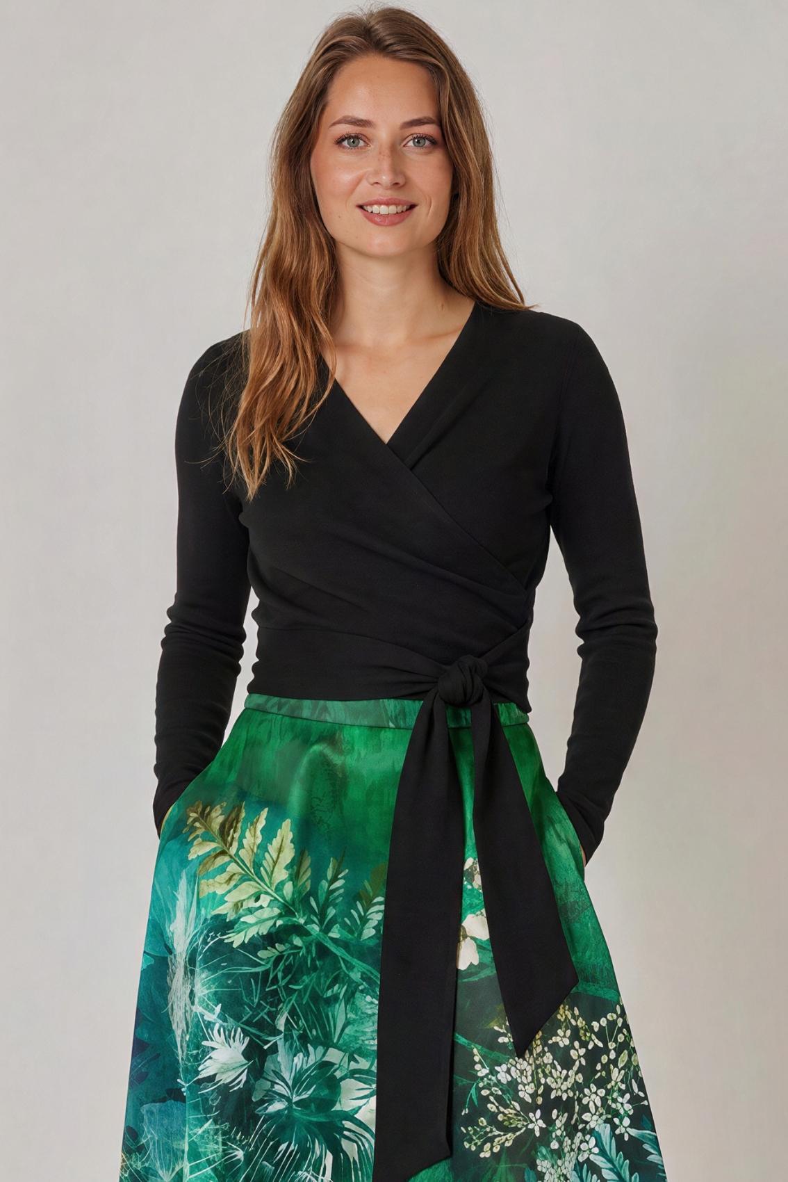 Model trägt Wickeltop in Schwarz mit gebundenem Taillengürtel, Frontansicht.
