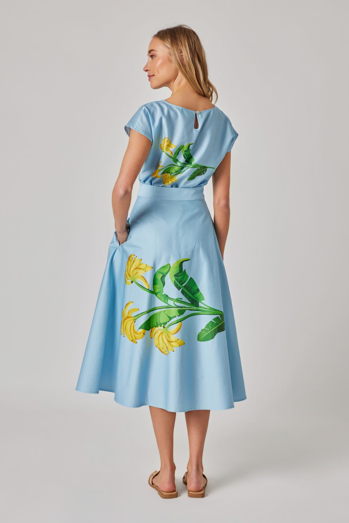 Model trägt hellblauen Midirock mit Bananen-Print in Rückenansicht, hoher Bund, Zip hinten.