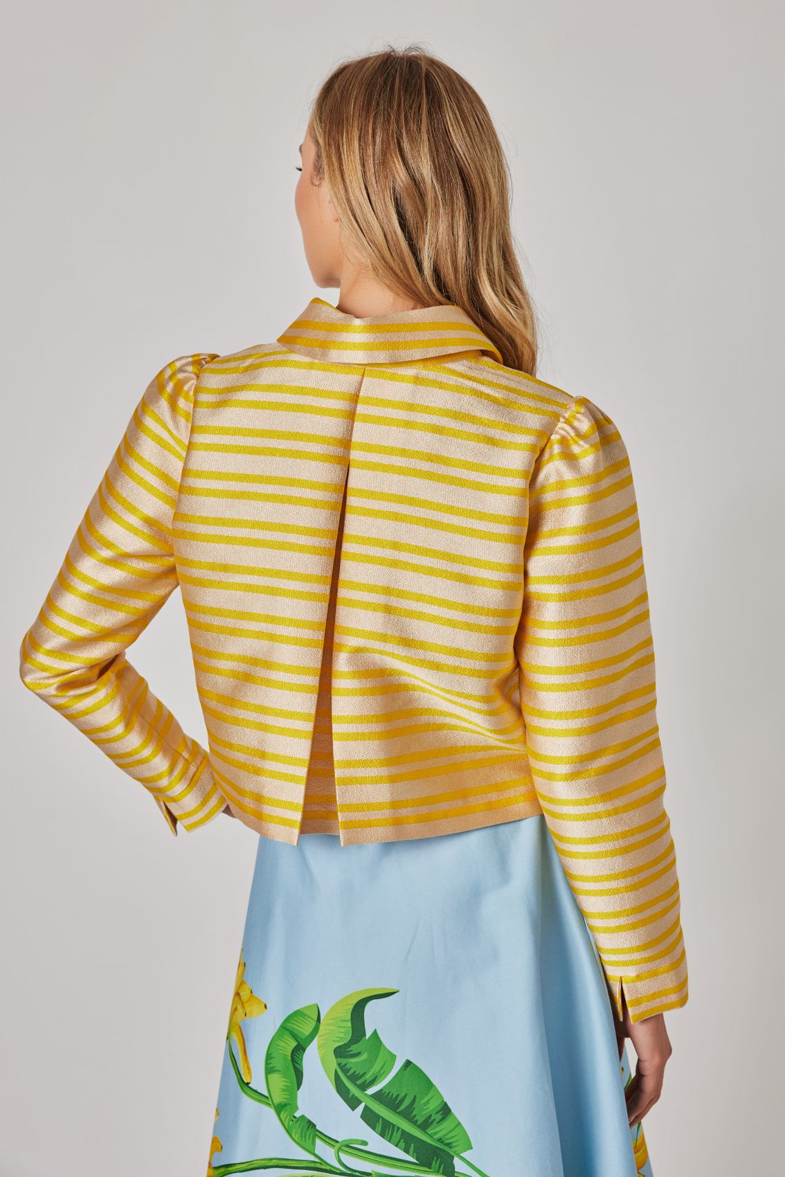Model trägt gestreifte Kurzjacke in Gold-Gelb in Rückenansicht, Kellerfalte für Bewegungsfreiheit.