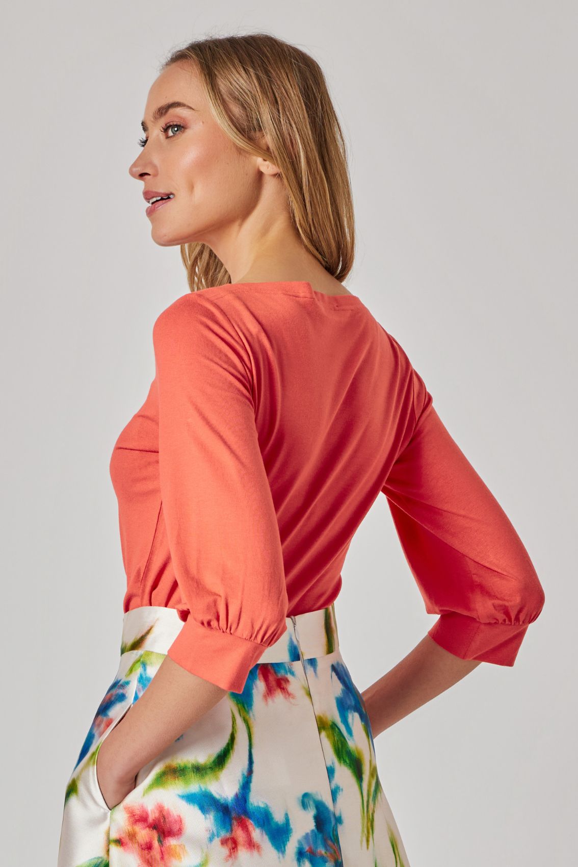 Model trägt orangefarbenes Shirt mit Manschettenärmeln, Rückenansicht, cleanes Design und U-Boot-Ausschnitt.