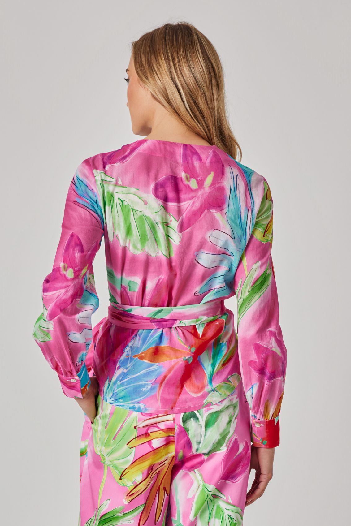 Model trägt pinkes Wickeloberteil mit langen Ärmeln und Aquarell-Blumenprint, Rückenansicht.