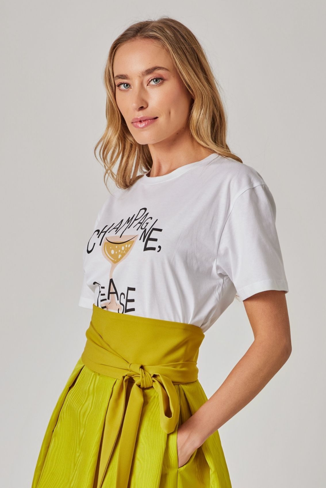Model trägt weißes T-Shirt mit Print und gelbem Rock mit Bindegürtel, Seitenansicht.