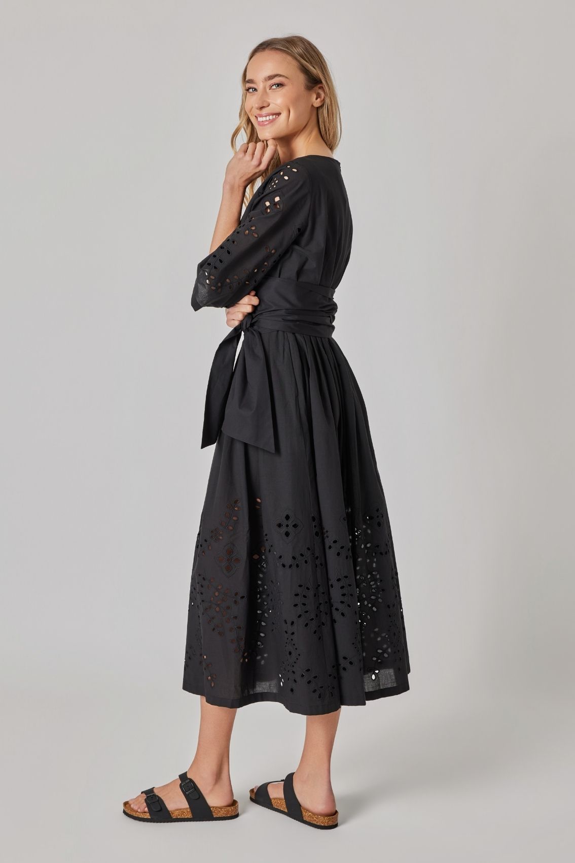 Model trägt schwarzes Midikleid mit tailliertem Bindegürtel und Lochstickerei an den Ärmeln.