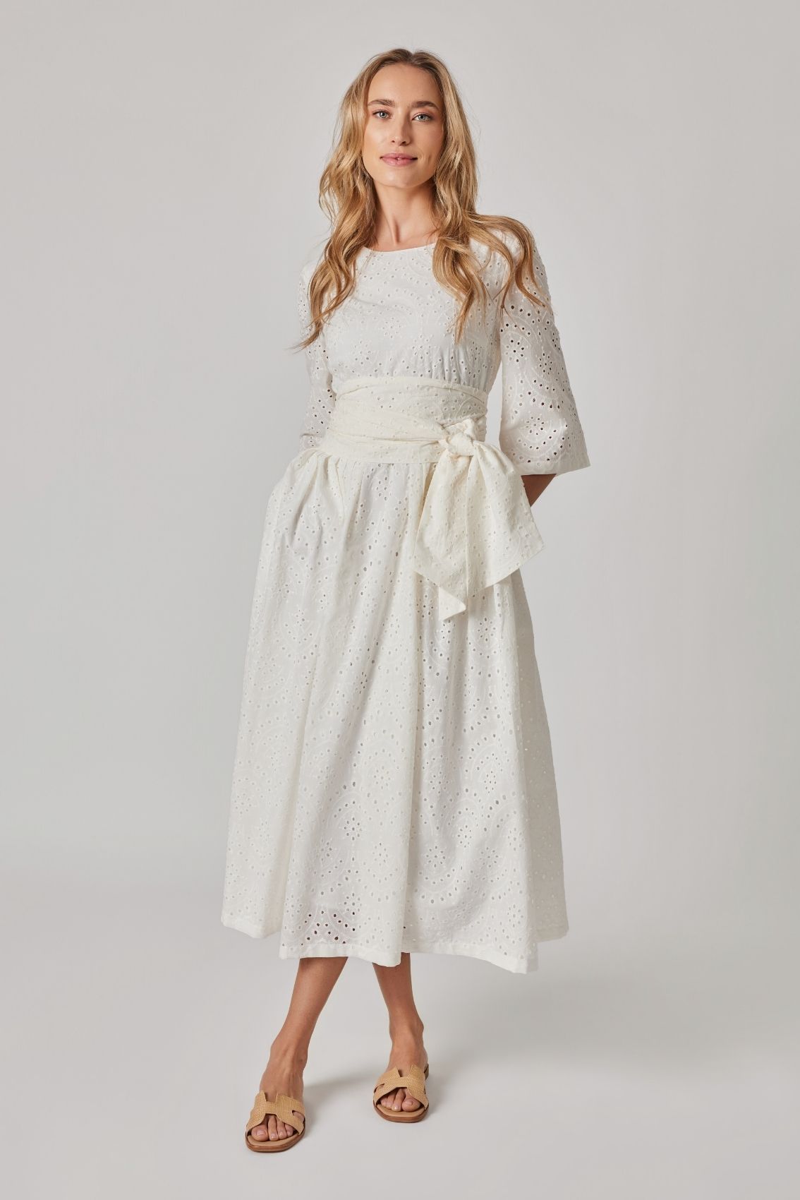 Model trägt weißes Broderie Midikleid mit Bindegürtel, 3/4-Ärmeln und weitem Rock, Frontansicht.