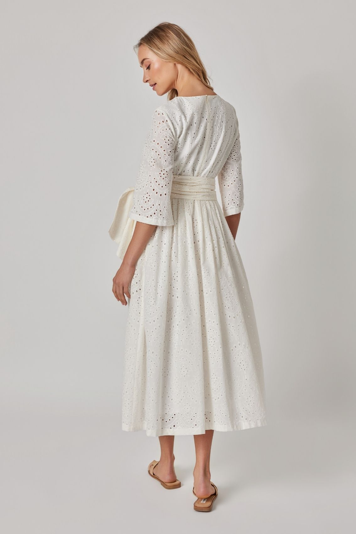 Model trägt weißes Broderie Midikleid mit 3/4-Ärmeln und Reißverschluss hinten, Rückenansicht.