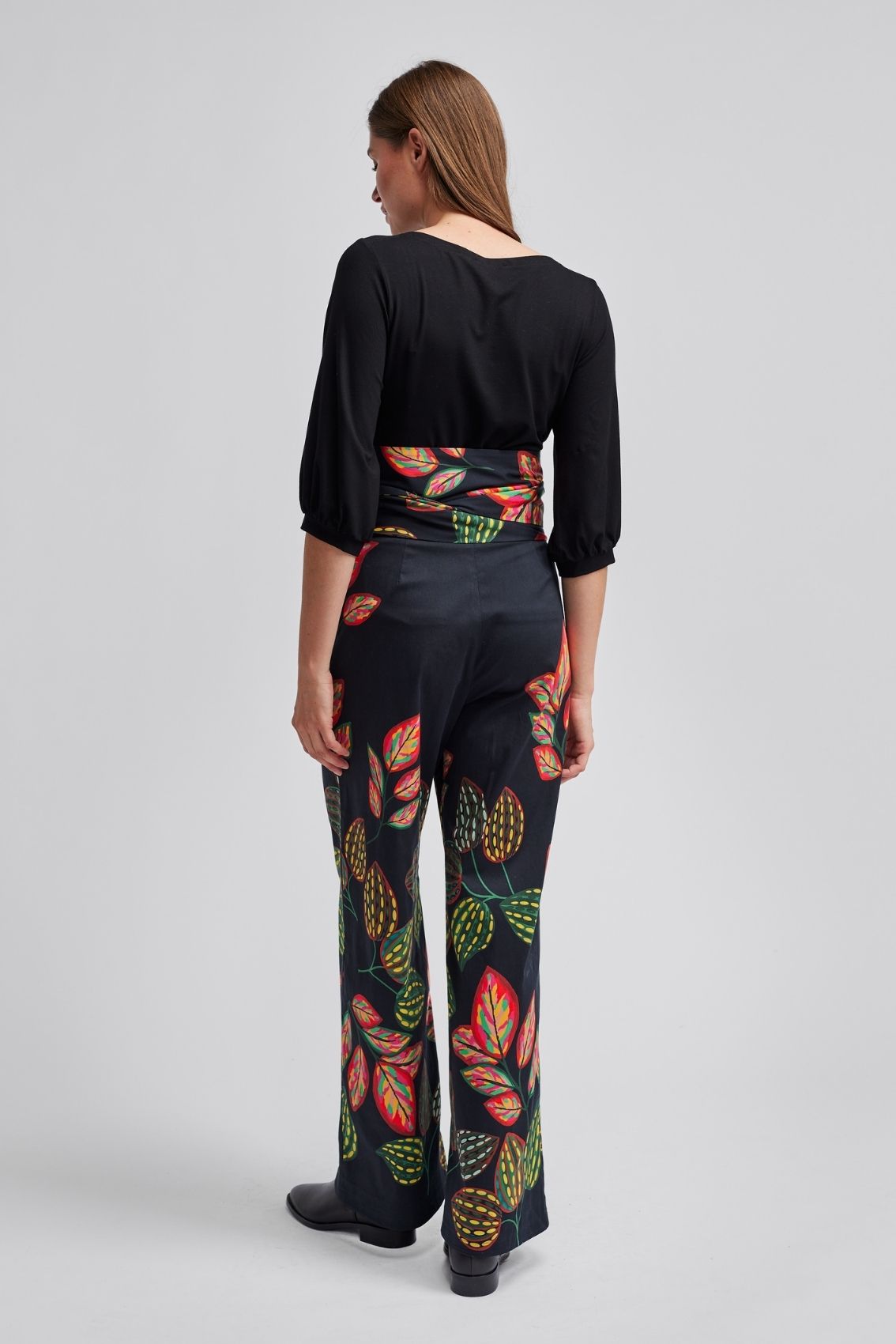 Model trägt schwarze High-Waist Hose mit weitem Bein, Rückenansicht mit buntem Blätter-Print.