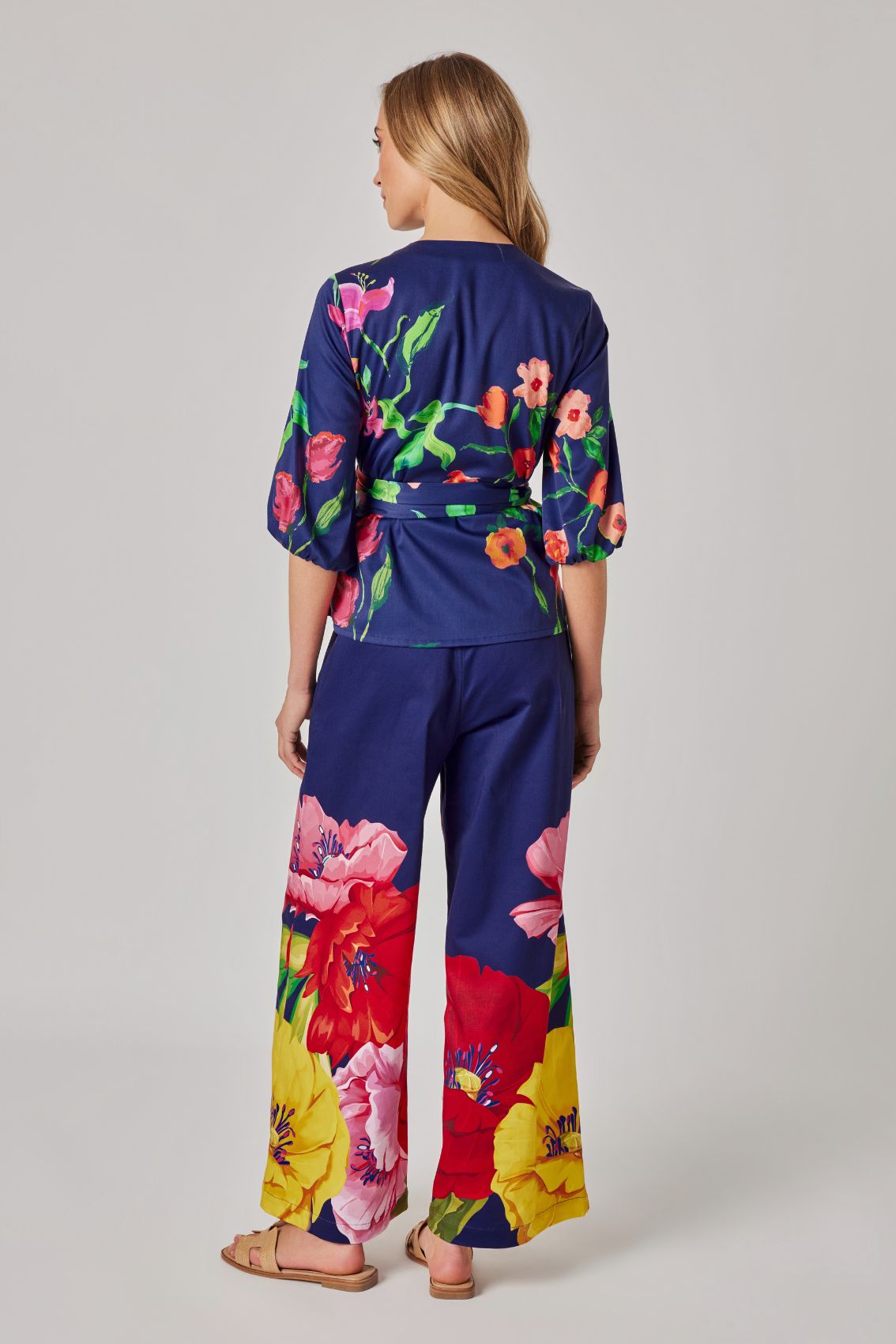 Model trägt dunkelblaue Hose mit weitem Bein und großflächigem Blumenprint, Rückenansicht.