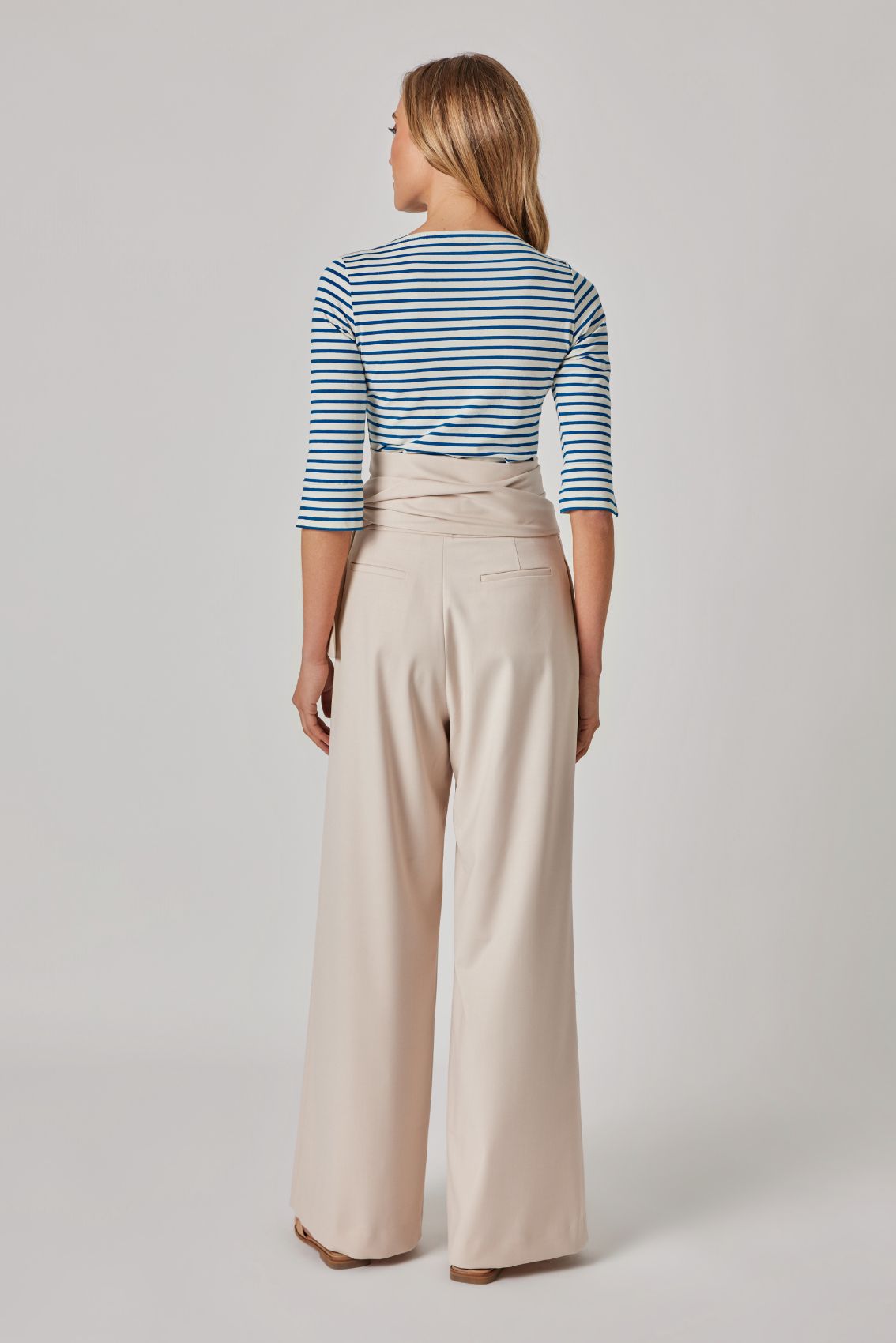 Model trägt gestreiftes 3/4-Arm Top und beige, weite Hose mit Wickelbund, Rückenansicht.