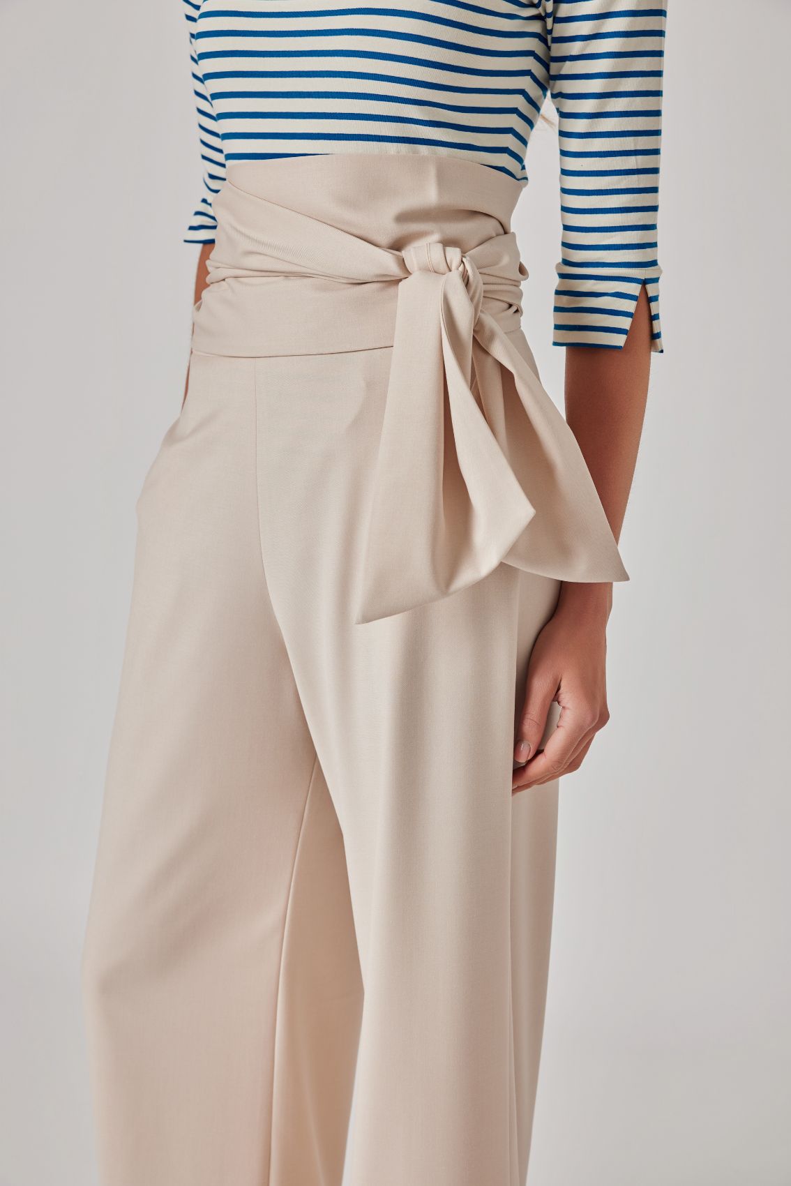Close-up: beige, hoch geschnittene Hose mit breitem Wickelbund und seitlich gebundenem Bindegürtel.